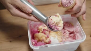 Kadın pembe dondurma toplarını toplar ve onları birbiri üstüne istifler waffle külahında..