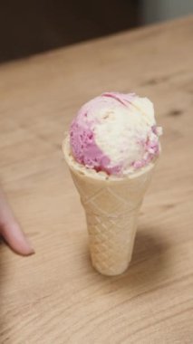 Kadın özel bir kaşıkla dondurmayı kutudan topluyor ve yanında da pembe bir dondurma külahıyla waffle külahı var. Dikey video.
