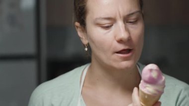 Genç bir kadın ev ortamında gözleme külahını pembe dondurmayla yalıyor..