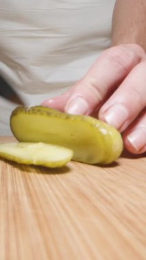 Beyaz önlüklü kadın kesim tahtasındaki salatalık turşusunu kesiyor. Dolly Slider aşırı yakın çekim. Dikey video.