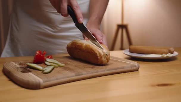 女人把热狗包切成薄片 旁边放些蔬菜在里面 — 图库视频影像