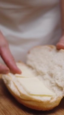 Kadın sosisli hazırlıyor, ekmeğin içine peynir ve domates dilimleri koyuyor. Dikey video.