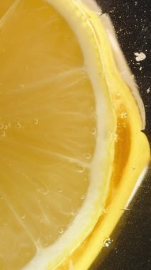Dikey video. Cam sehpanın üzerindeki limon diliminin alttaki görüntüsü. Bal damlıyor, yakın plan siyah arka plan üzerine..