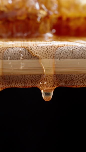 バーティカルビデオ ハニカムの天然蜂蜜は その滴が落ちている木製板の上にあります ドリースライダー極端なクローズアップ — ストック動画