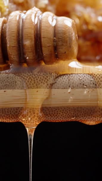 垂直录像 蜂窝中的蜂蜜放在木制的木板上 旁边有一个蜂蜜勺 在黑色的背景下滴下 滑翔机极端特写 — 图库视频影像