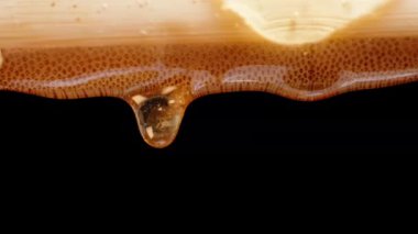 Bambu tahtasından damlayan bal damlaları, siyah arkaplana yakın çekim..