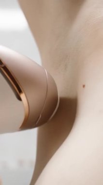 Dikey video. Koltuk altı fotokopisi: bir kadın ev epilatörü kullanarak saçlarını temizler, yakın çekim..