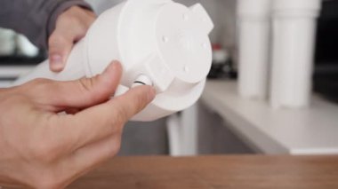Değiştirilebilir su filtreleri için beyaz bir ev. Bir adam hemen tüp için sökülebilir bir vida takar..