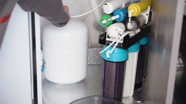 Ters osmoz membranlı filtre sistemi, bir adam depolama tankının vanasını çevirir ve su kazara bir çeşme gibi fışkırır. Hemen vanayı kapatıyor..