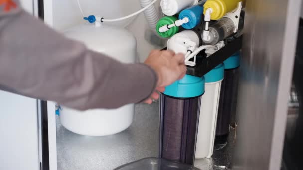 厨房水池下的过滤器 一个带有白色储罐的反渗透系统 一个人在拆管子 水倒进桶里 正在更换滤清器 — 图库视频影像