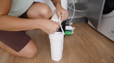 Genç bir kadın mutfağı için bağımsız olarak ters osmoz su filtreleme sistemi kurar ve filtre yuvasına tüpler yerleştirir..