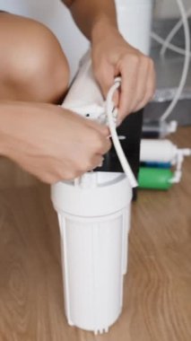 Dikey video. Genç bir kadın mutfağı için bağımsız olarak ters osmoz su filtreleme sistemi kurar ve filtre yuvasına tüpler yerleştirir..