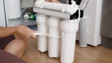 Bir kadın yerde otururken su filtresi sisteminin vidalarını söküyor..