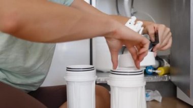 Bir kadın kendi mutfağında yerde otururken kendi başına su filtrelerini değiştiriyor..