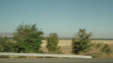 Araba yol boyunca hızla ilerliyor ve uzak dağların ve tarımsal alanların görüntülerini yakalıyorum..