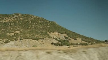 Dağlardan ve ağaçlardan oluşan hareket halindeki bir arabanın görüntüsü. Açık güneşli hava.