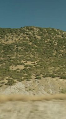 Dikey video. Dağlardan ve ağaçlardan oluşan hareket halindeki bir arabanın görüntüsü. Açık güneşli hava.