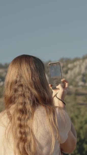 垂直录像 一位年轻女子在她的手机上为社交媒体拍摄美丽的风景 背景是高山和树木 — 图库视频影像