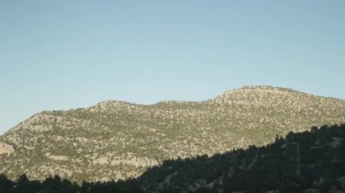 Ben yol boyunca giderken batan güneşin aydınlattığı seyrek çalılarla kaplı yüksek tepeler..
