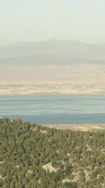 Dikey video. Dağlarda arabayla seyahat ederken, dağların arkasında geniş bir göl manzarası..