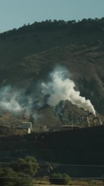 Dikey video. Arka planda dağlar olan yol kenarındaki kafe ve bacadan çıkan kalın beyaz duman. Hareket eden bir arabadan görünüm.