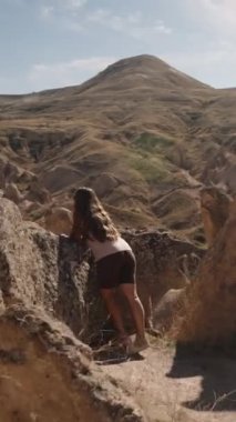 Dikey video. Kamera, Antik Hayal Vadisi 'ndeki bir taşın yakınındaki manzaraya hayran olan genç bir kadına yaklaşıyor..