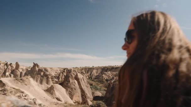 若い女性は古代の石の近くの古い都市の古代の岩の景色を賞賛しています そして彼女は彼女の手でどこかを指しています — ストック動画
