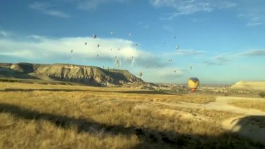 Gün batımında, Kapadokya 'da bir tarladan geçeceğiz, ve uzak mesafede, sıcak hava balonları dağların üzerinde uçuyor olacak..