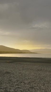 Gün batımında, güneş dağın arkasında batar ve güneş ışığı bulutların arasından parlar göldeki suya, panorama.