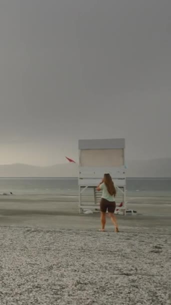 多云的天气 太阳几乎落在了山后 但尽管即将下起雨来 一位年轻的女子仍向湖面走去 — 图库视频影像