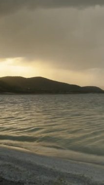 Göl üzerinde Fırtına Bulutları Toplanıyor ve Dağların Önündeki Uzaktan Yağmur Yaklaşıyor. Güneş hala görünür, ama dağın arkasında batıyor. Kasvetli atmosfer.