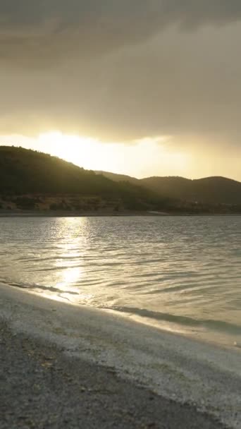 日落时 在高山湖岸上 太阳的最后一道光芒穿过高山 冲破汹涌的云彩 照亮了水面 — 图库视频影像