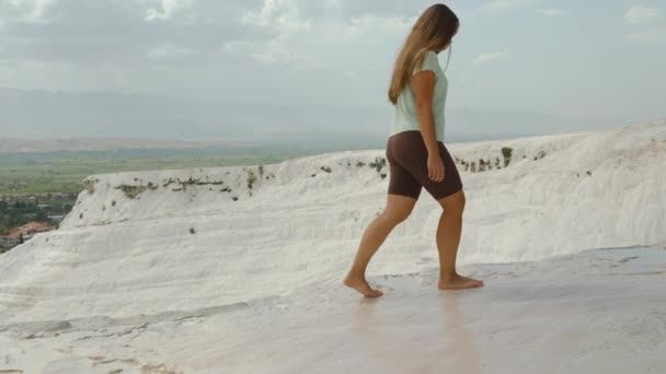 白いパムカレトラバーチン 若い女性は崖の端に裸足を歩き 明るい日 ユニークな場所を探索しています スローモーション — ストック動画