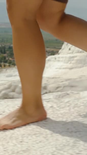 垂直录像 在帕穆克卡莱 一位年轻女子赤脚行走在白岩的边缘 背景是美丽的白山风景和山脚下的湖水 慢动作 — 图库视频影像