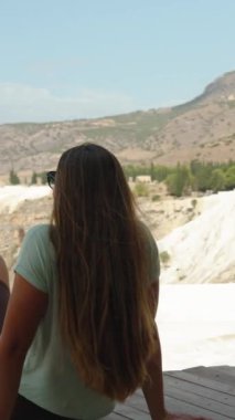 Dikey video. Beyaz Dağ 'ın tepesinde kalsiyumdan oluşmuş genç bir kadın bir köprüde oturuyor ve yüksek irtifa manzarasının tadını çıkarıyor. Dünya 'daki inanılmaz yerleri keşfediyorum..