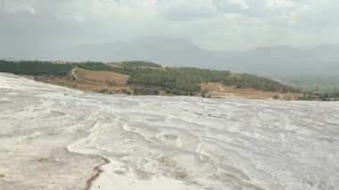 Zirvede, Pamukkale 'nin Beyaz Travertines manzarası, su olmadan kurumuş küçük doğal havuzlar. Dağın eteğinde bir şehir.