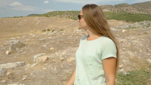 若い旅の女性は 山の背景と破壊された都市の古代の石に対して道を下ります — ストック動画