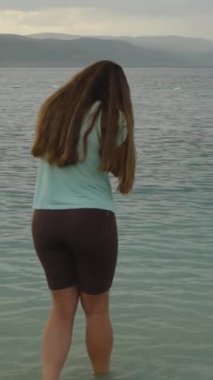 Dikey video. Dağ Gölü 'nün üzerindeki bulutlu hava. Suda üzgün bir genç kadın duruyor..