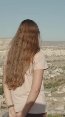 Dikey video. Uzun saçlı genç bir kadın tek başına seyahat ediyor, Goreme, Türkiye 'deki doğal parkın manzarasına hayran, panoramik bir çekim..
