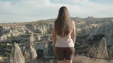 Kahverengi şortlu genç bir kadın Goreme, Türkiye 'nin doğal parkındaki antik kente bakıyor, panoramik manzara.