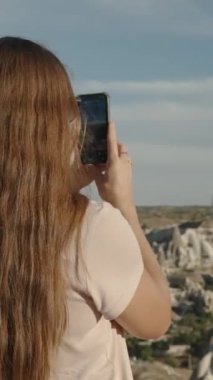 Dikey video. Genç bir kadın, Türkiye 'deki Goreme doğal parkının panoramik manzarasını telefonunda geziyor ve güzel hava görüntülerini yakalıyor..