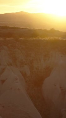 Dikey video. Gün batımında beyaz taştan bir kanyonun panoramik görüntüsü, kenarında oturan genç bir kadın, uzaklığa bakıyor..