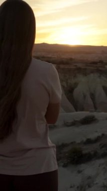 Dikey video. Yalnızlık kavramı. Elleri bağlı genç bir kadın beyaz bir taş kanyonun kenarında gün batımını izliyor..