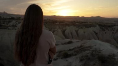 Uzun saçlı genç bir kadının arkasından bakıldığında güneş neredeyse uzak dağın arkasında batıyor ve günbatımının tadını çıkarıyor..