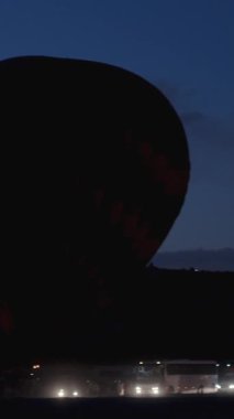 Dikey video. Şafakta sıcak hava balonu fırlatma alanı. Kalkış için hazırlıklar devam ediyor. Birçok sıcak hava balonu eş zamanlı kalkış için hazırlanıyor..