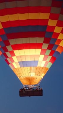 Dikey video. Çok renkli dev bir sıcak hava balonu sepette insanlar var, uçuş sırasında yakın çekim. Yangın bazen içeride alevlenir..