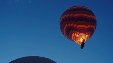 Şafakta, gökyüzünde hala görünen yıldızlarla, devasa bir sıcak hava balonu içeriden alevler salıyor ve yukarıya doğru yükseliyor. Sepetin içindeki insanlar yükseklikten manzaranın tadını çıkarıyorlar. Havada düzinelerce balon.