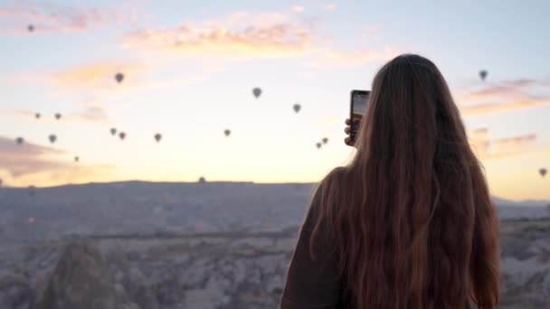 日出时 一位妇女站在山顶上 看到许多热气球在峡谷中飞舞 — 图库视频影像
