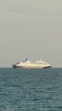 Dikey video. Uzak bir denizde batan güneşli bir yolcu gemisi..