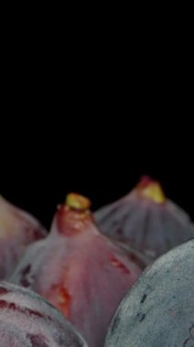 Dikey video. Olgun Koyu Mavi İncir meyveleri bir masanın üzerine dizilmiştir. Siyah arka plana karşı. Dolly kaydırıcı aşırı yakın çekim.